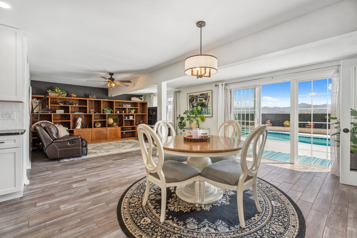 Dining room and family room with wood floors, large white built in bookcase and a sliding glass door with a view out to the pool and backyard.
