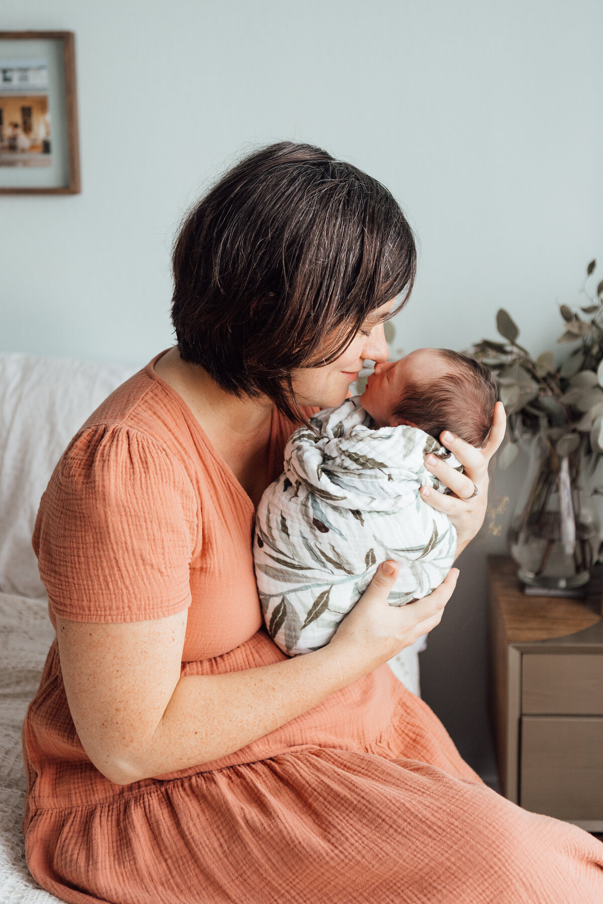 Stephanie snuggles her newborn  son who is wrapped in an olive leaf swaddle