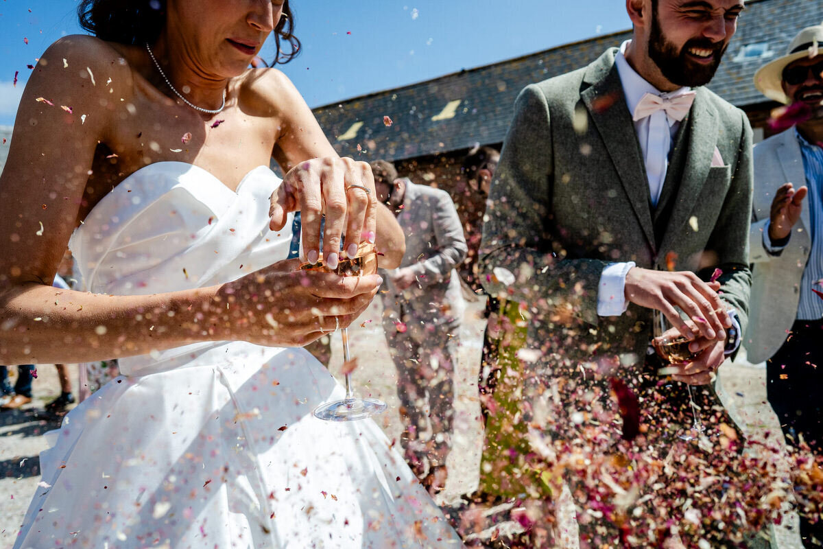 confetti photograph, close up of bride and groom walking down the line covering the wine glasses wiht their hands to stop confetti getting in.