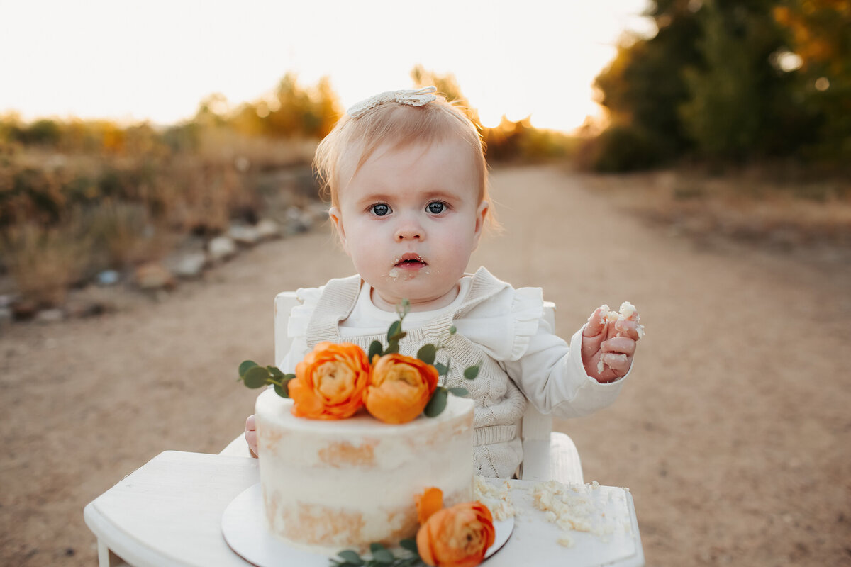 a little girl eating a pretty cake with flowers at sunset outdoors in denver for her first birthday
