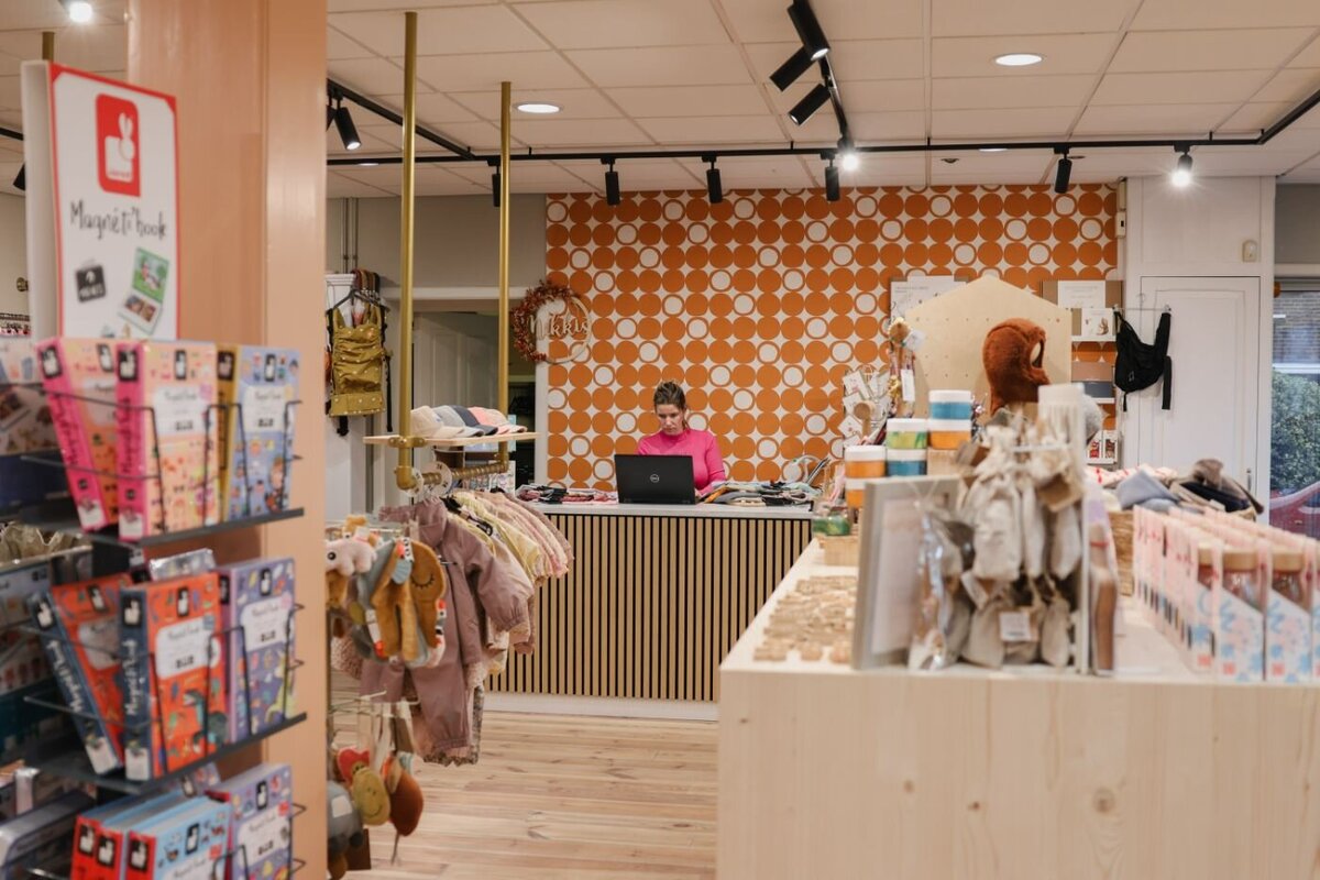 Een winkelinterieur met kledingrekken en een medewerker die achter de toonbank op een laptop werkt