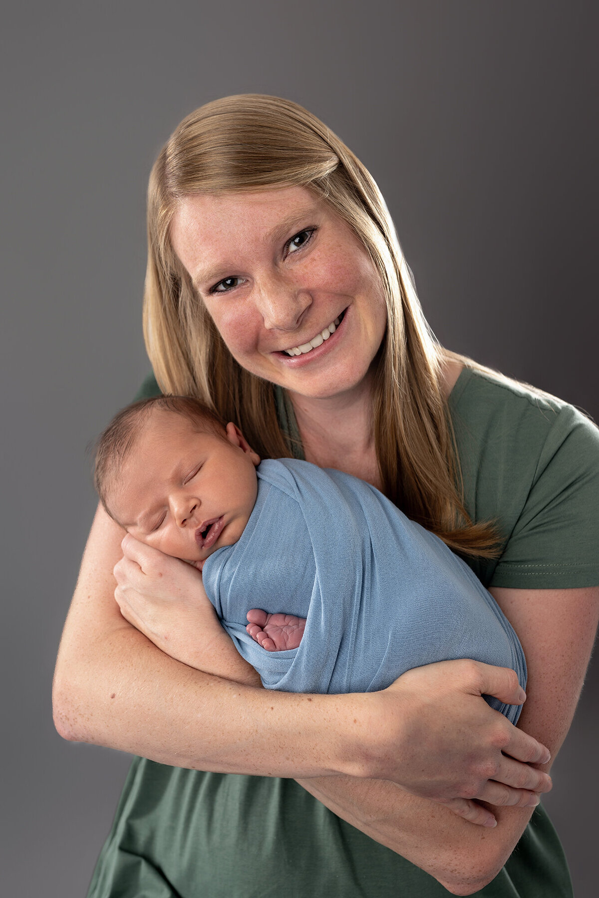 A happy mom cradles her newborn in a studio in a blue swaddle