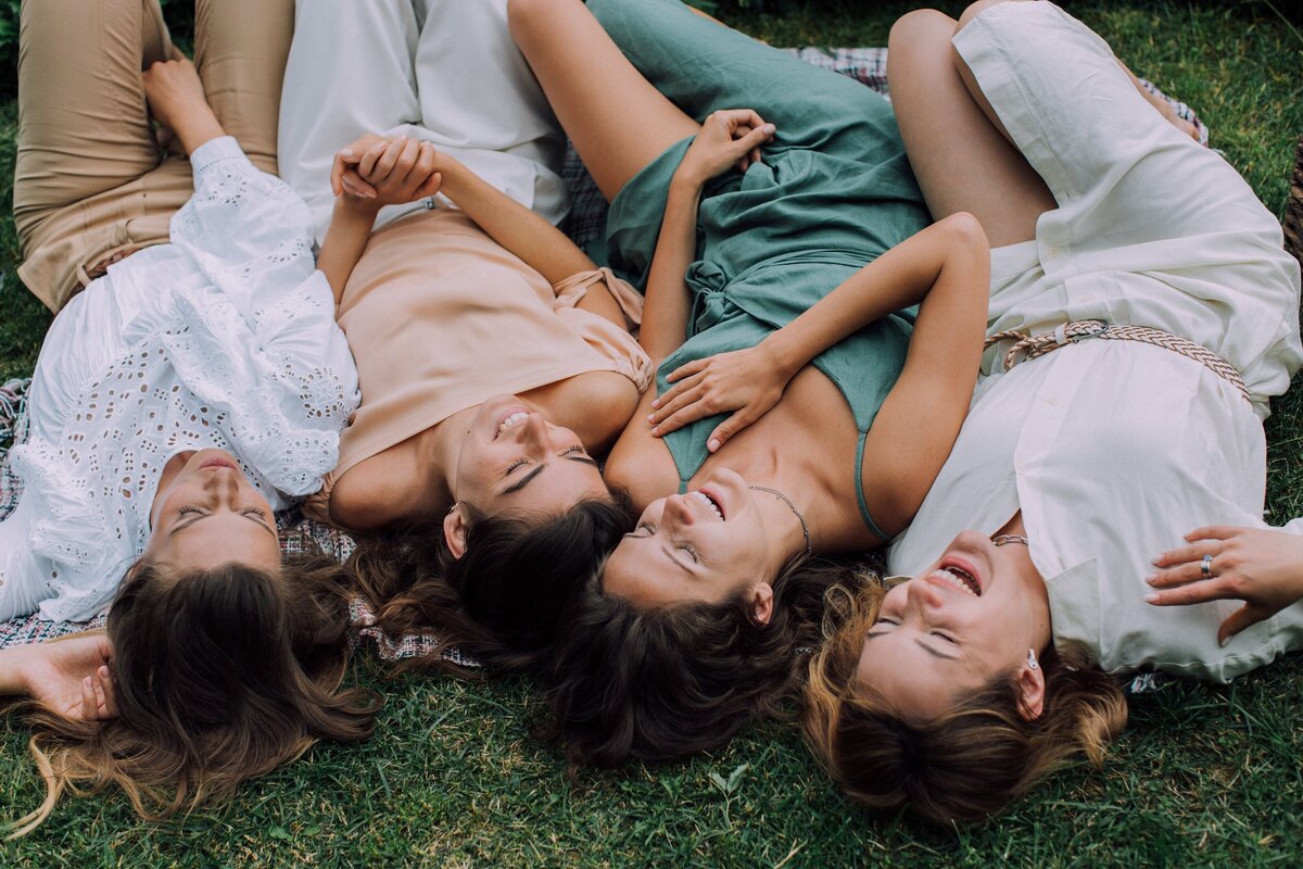 Four women in dresses laying on the grass laughing.