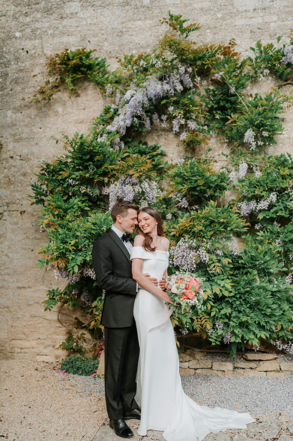 Bride and groom standing in front of the wisteria-covered wall at Caswell House