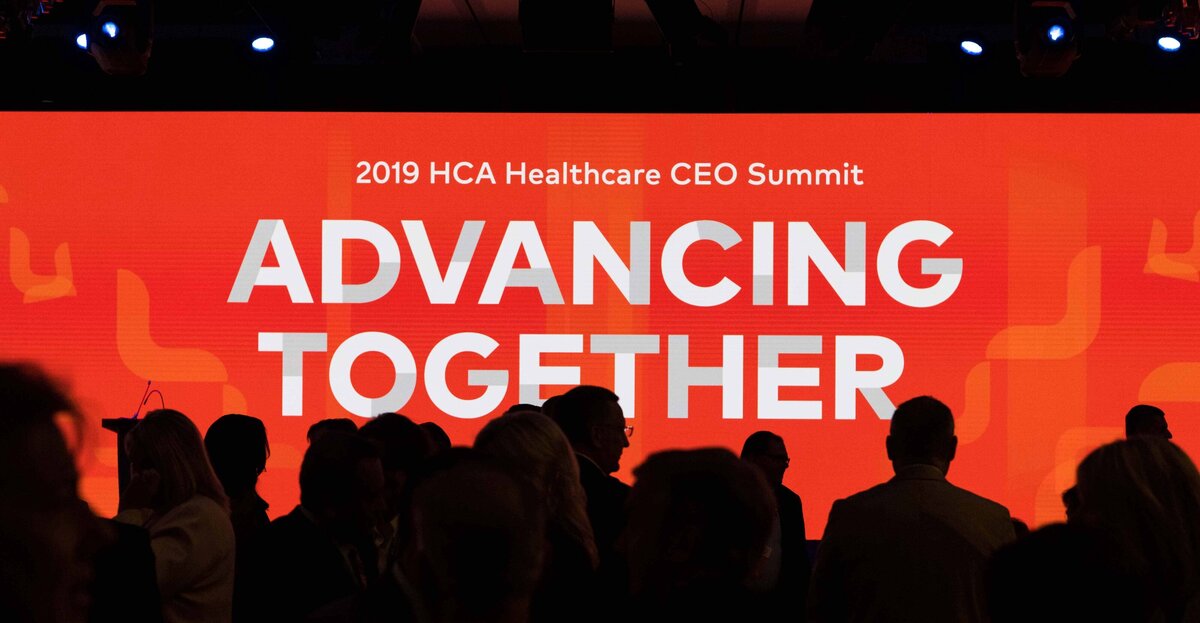 A crowd silhouetted on a large screen at HCA CEO Summit
