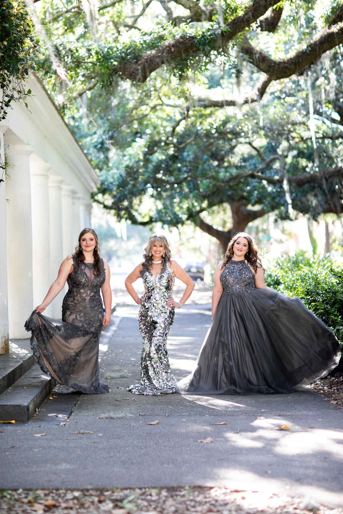 mother and daughters in glamorous gowns under trees