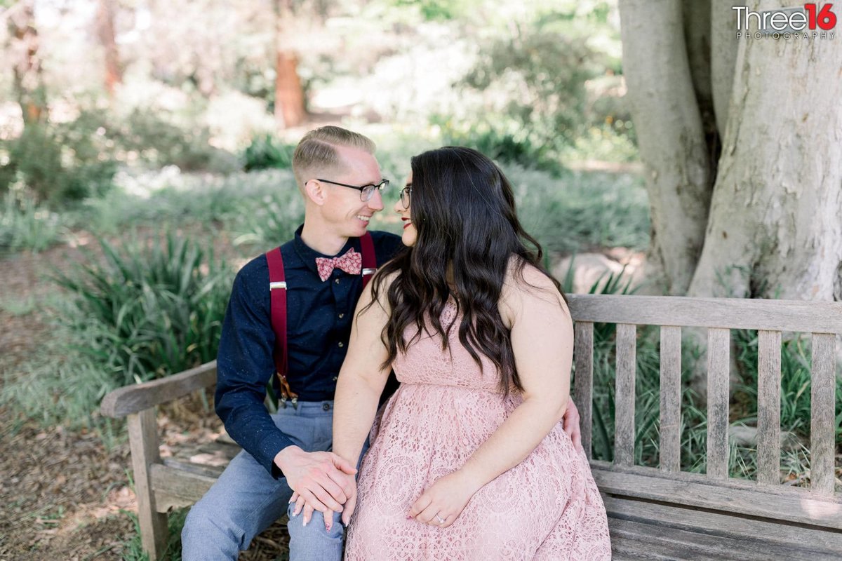 Engaged couple gaze into each other's eyes while sitting on a bench together