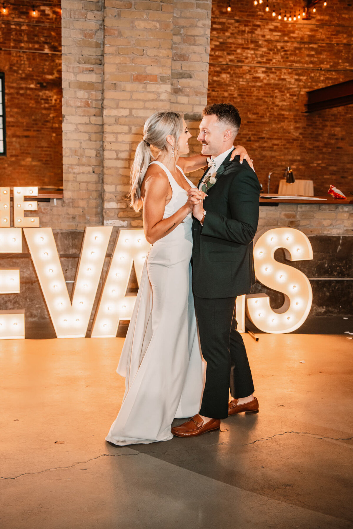 bride and groom dance in front of marquee letters of their last name
