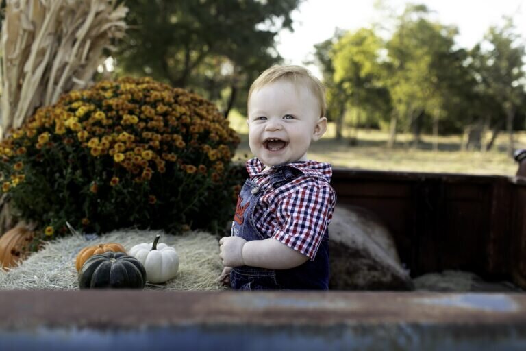 Birthday child sitting on a pumpkin, surrounded by autumn colors and pumpkins, enjoying a fun photoshoot at the pumpkin patch