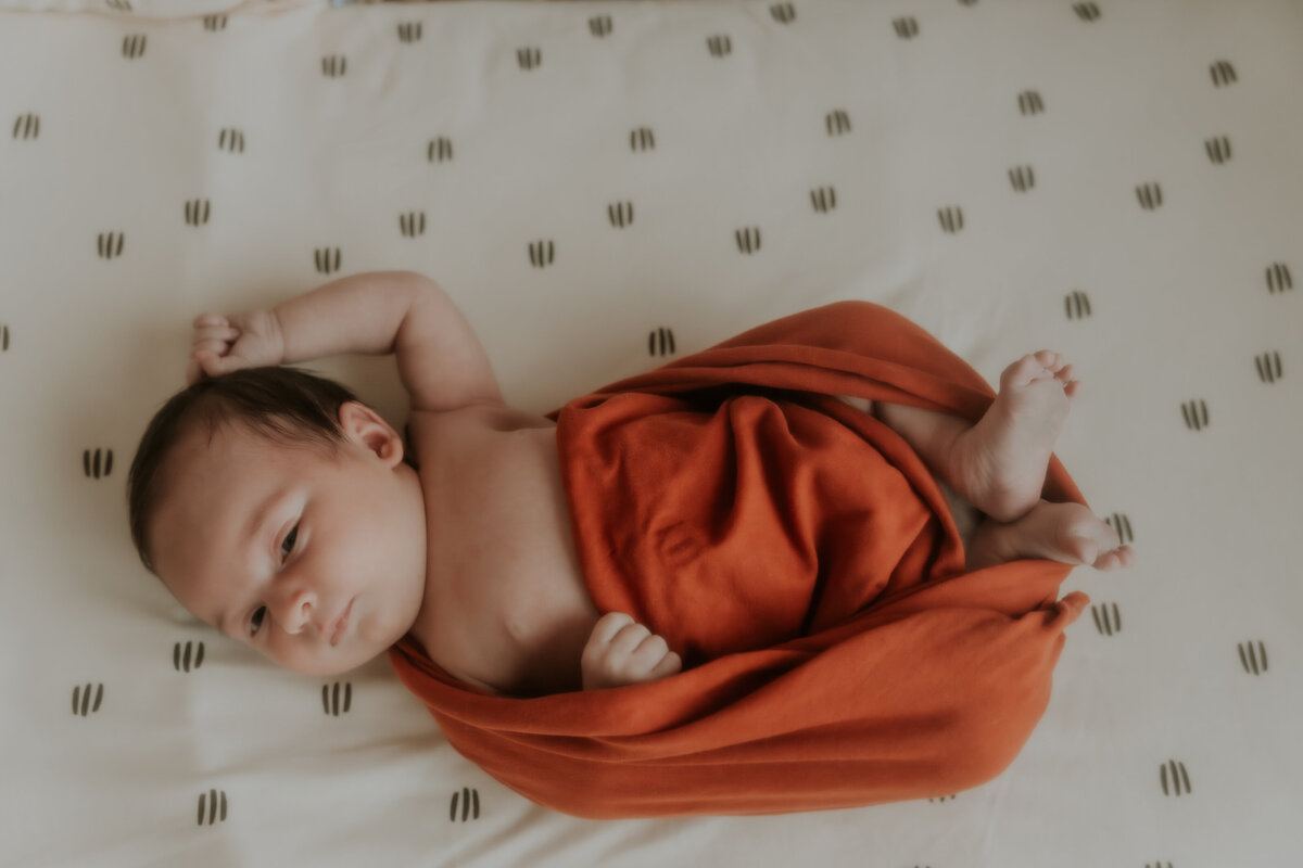 Newborn wrapped in een zachte wrap in de kleur roest. 