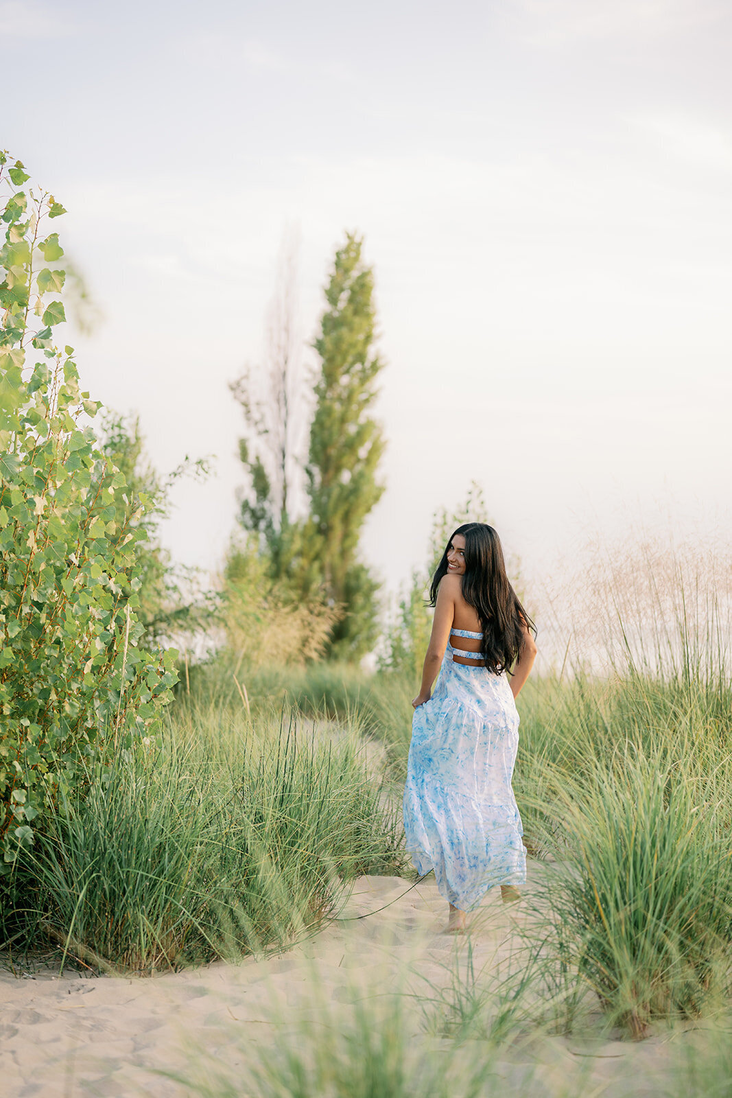 Senior girl smiling while sitting in dune grass at South Haven North Beach during her Lake Michigan senior photos.