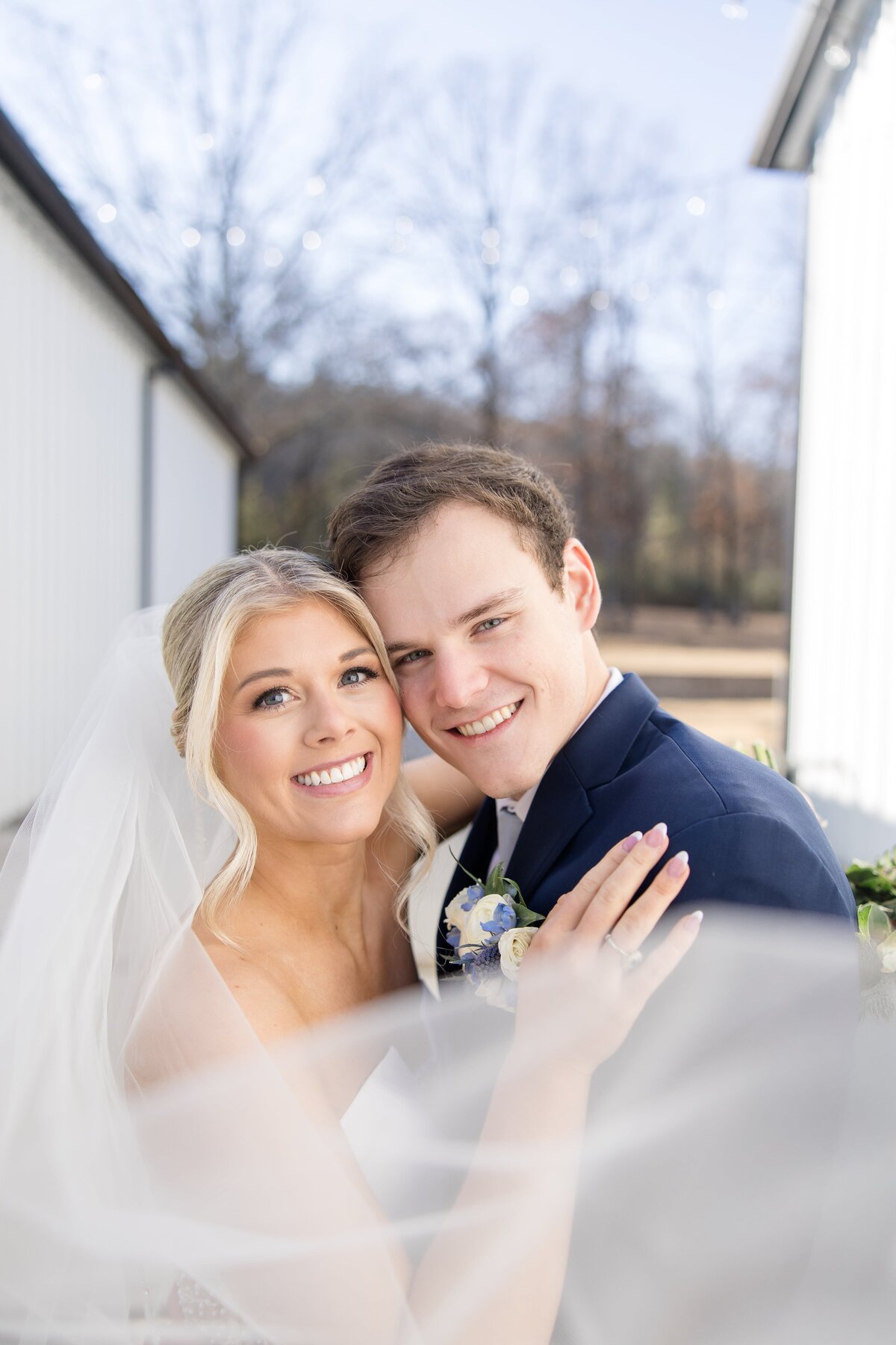 A happy newlywed couple hug and smile cheek to cheek with the veil wrapping around them in the wind for an Arkansas wedding photographer