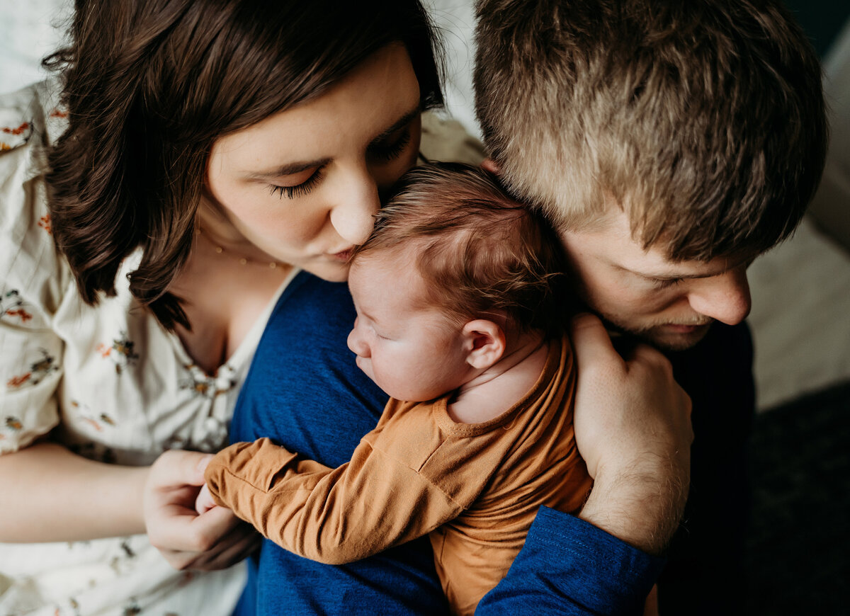 Newborn Photographer, dad holds new baby, as mom kisses her new son