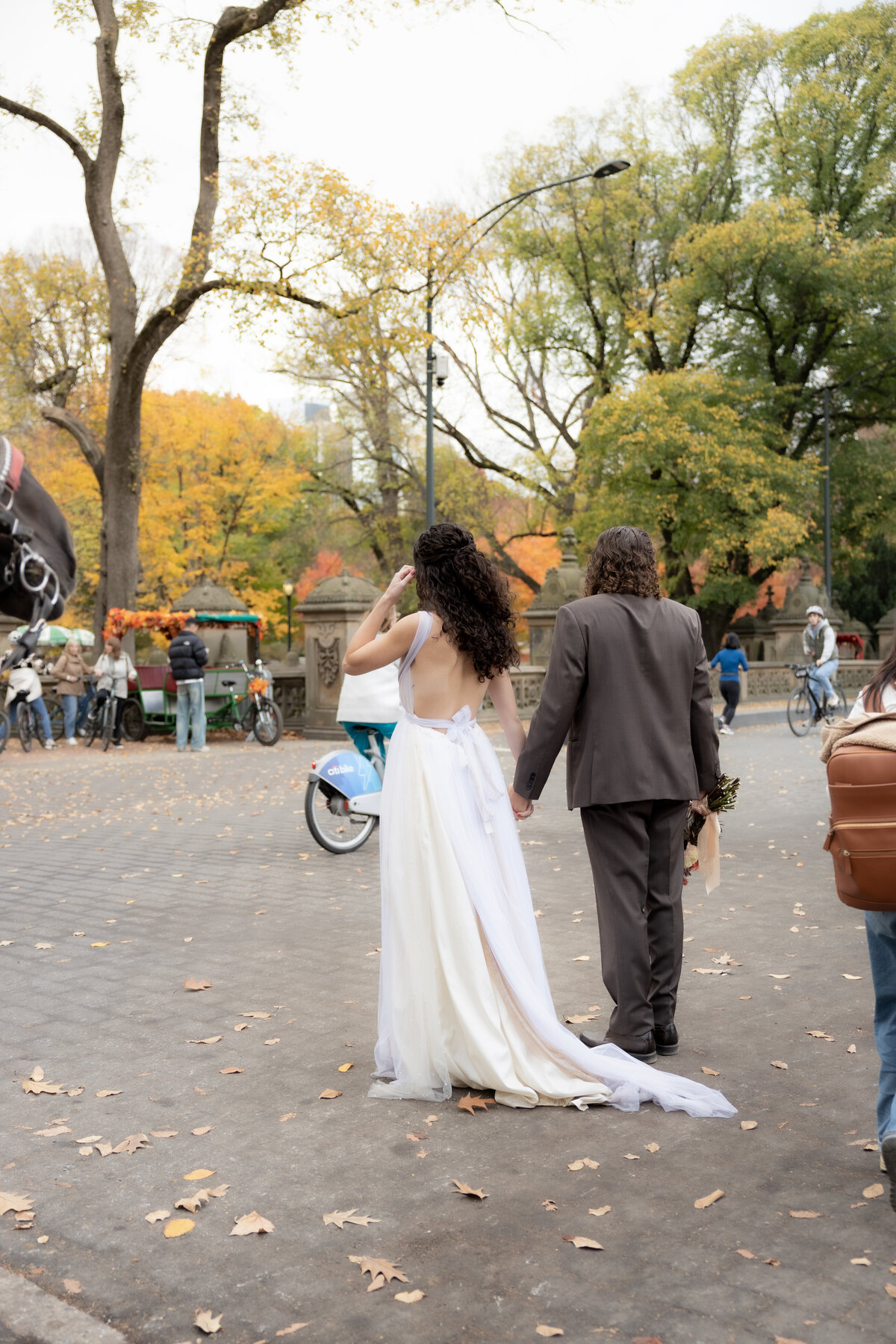 The bride laughing joyfully while holding her bouquet among autumn leaves in Central Park.