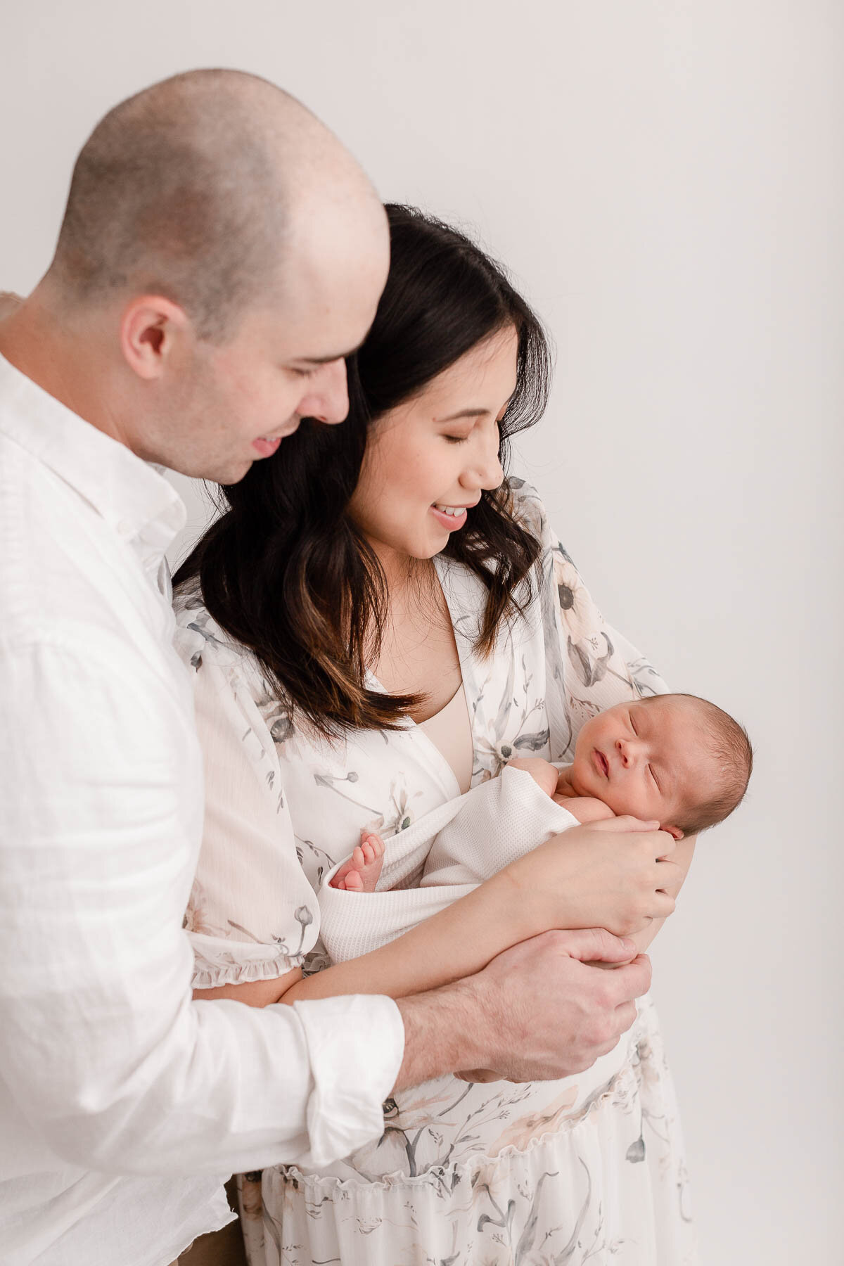 New parents holding newborn baby smiling and looking down at baby.