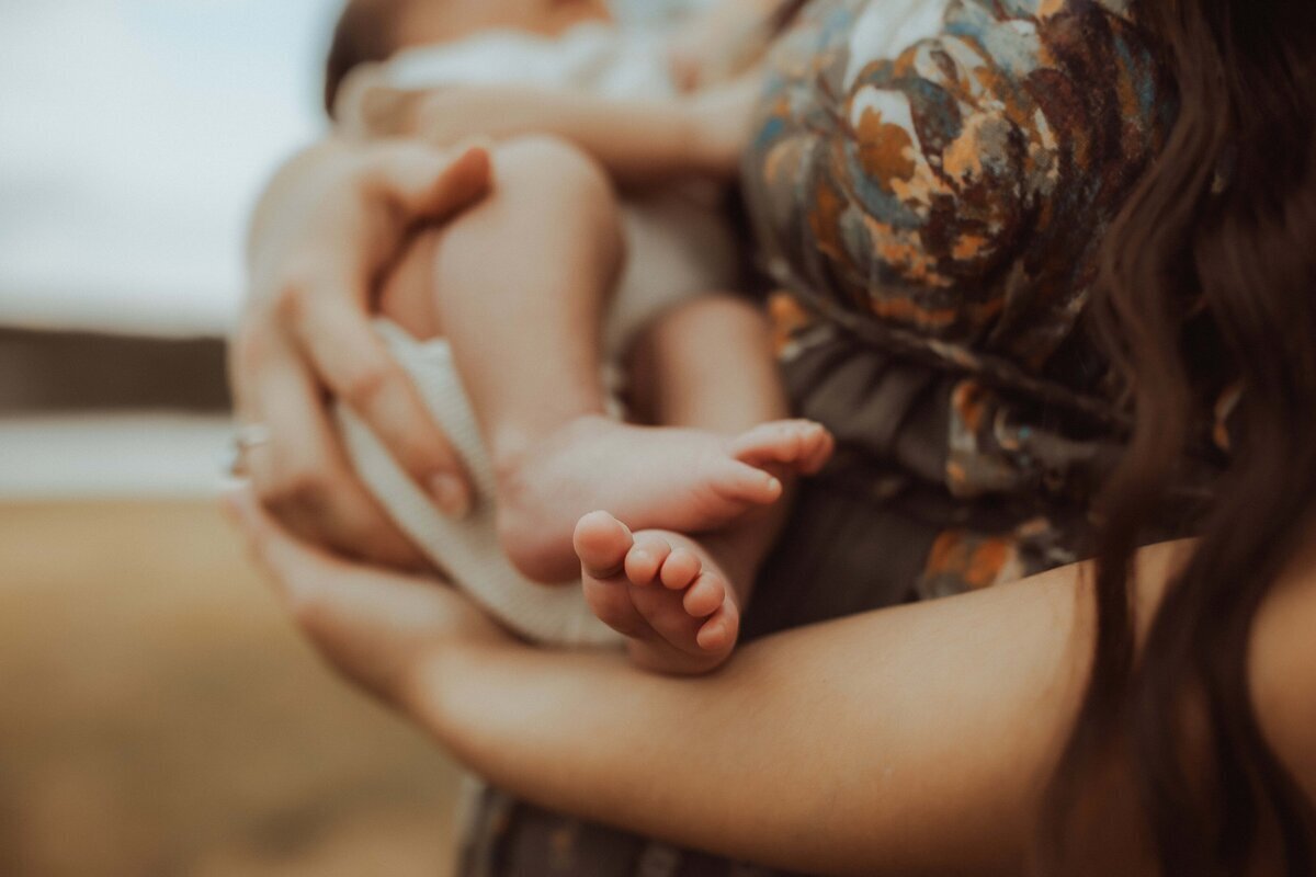 A Macon newborn photographer captures a tender moment as a person cradles a baby in a vibrant patterned garment, highlighting the infant's tiny feet.