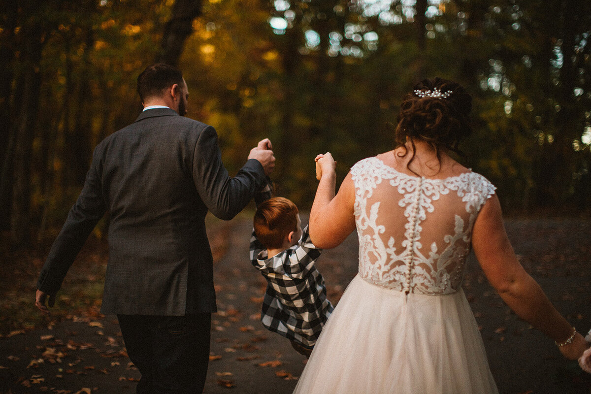 bride and groom walk away while swinging child in between them