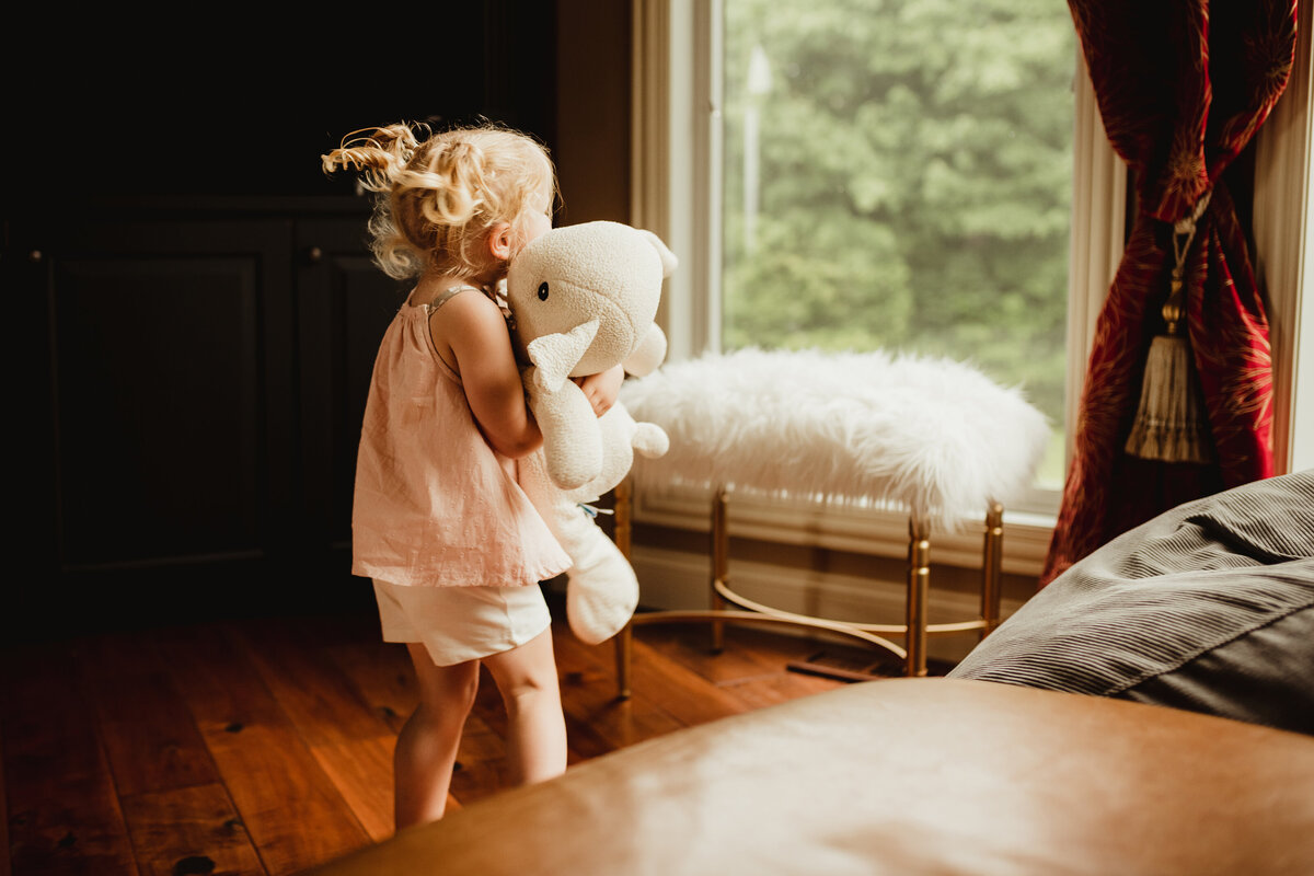 A little girl twirls her stuffed lamb in the living room.