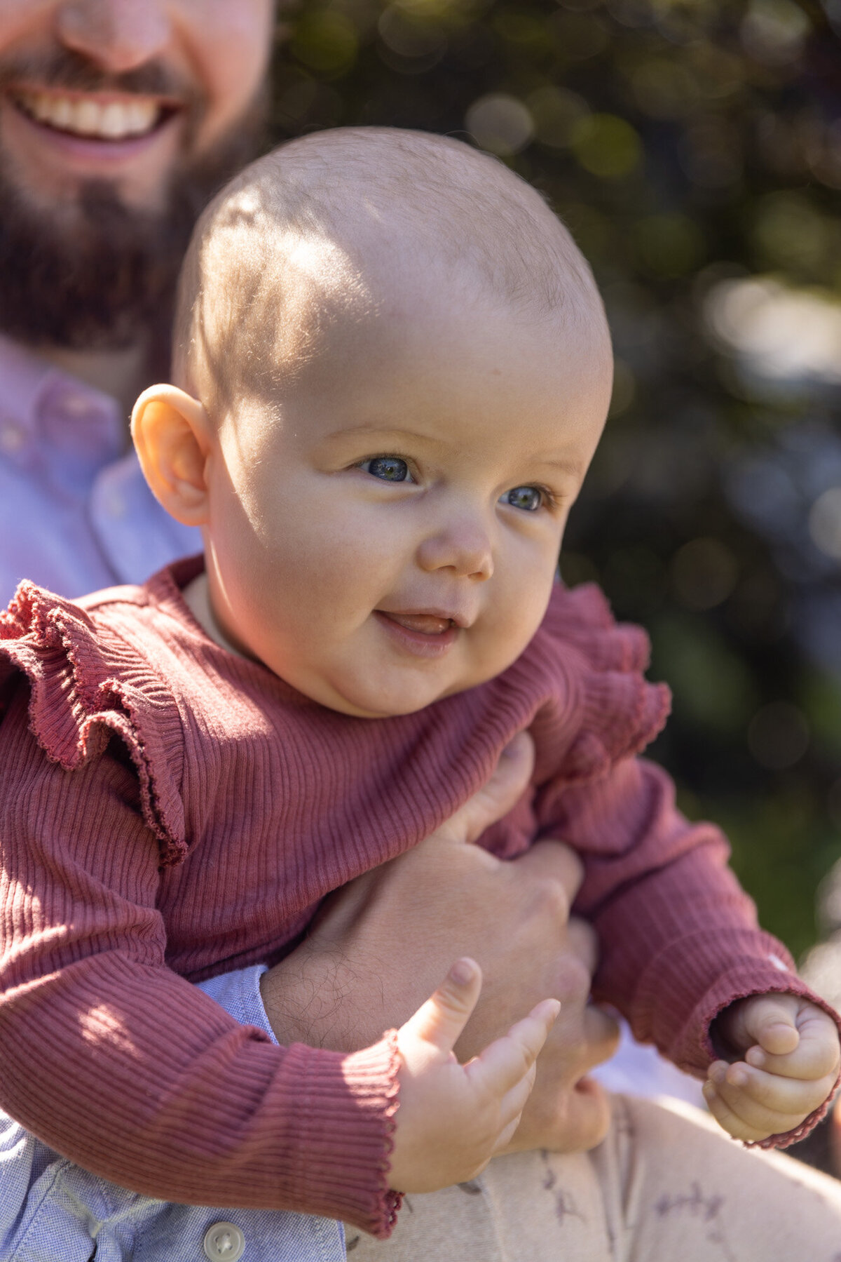 Nærbilde av baby som blir holdt av en mann. Man ser smilet til mannen i bakgrunnen.