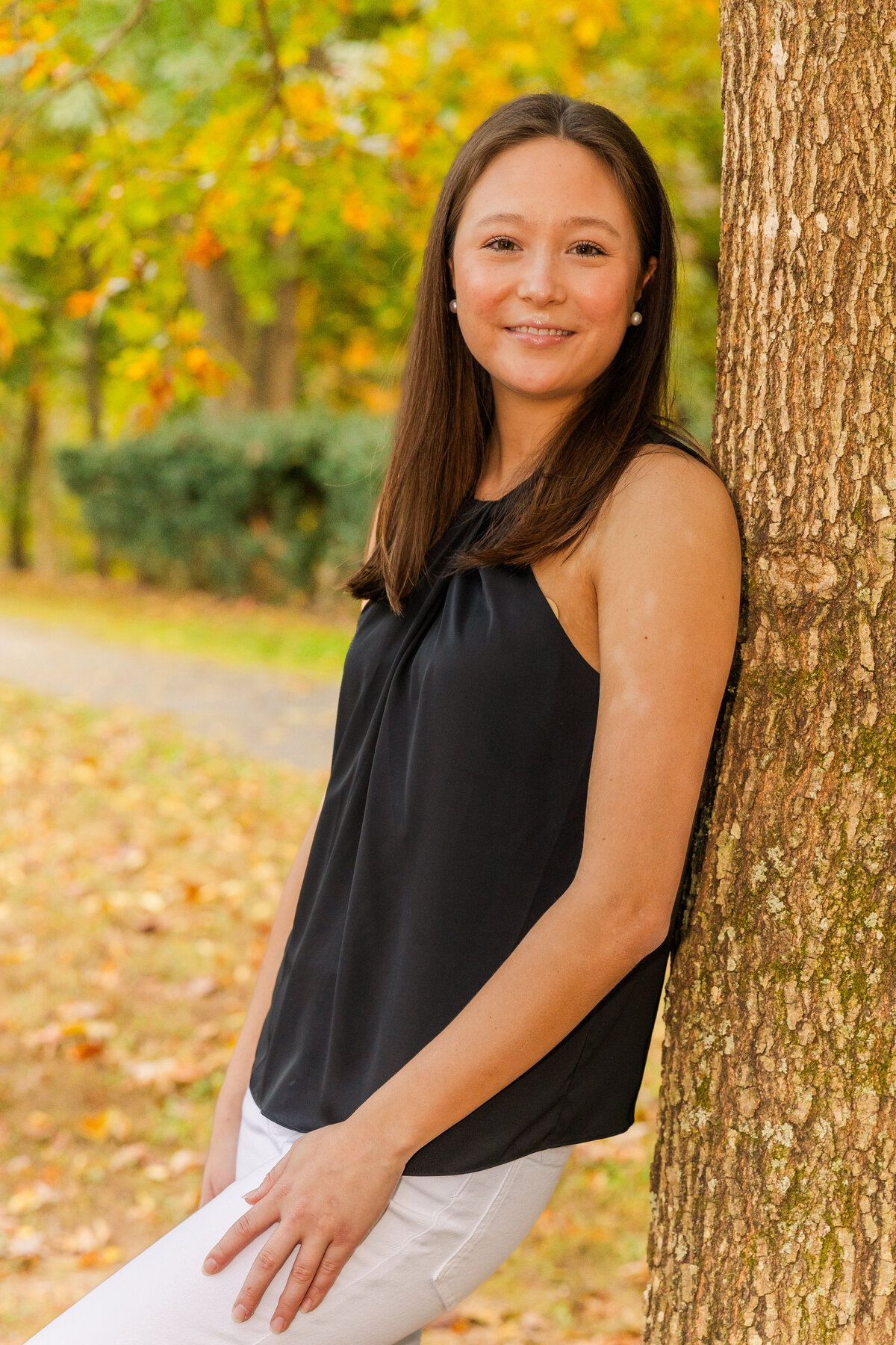 teenage girl wearing white jeans and black top leaning against a tree during senio photo session in Atlanta with Laure Photography