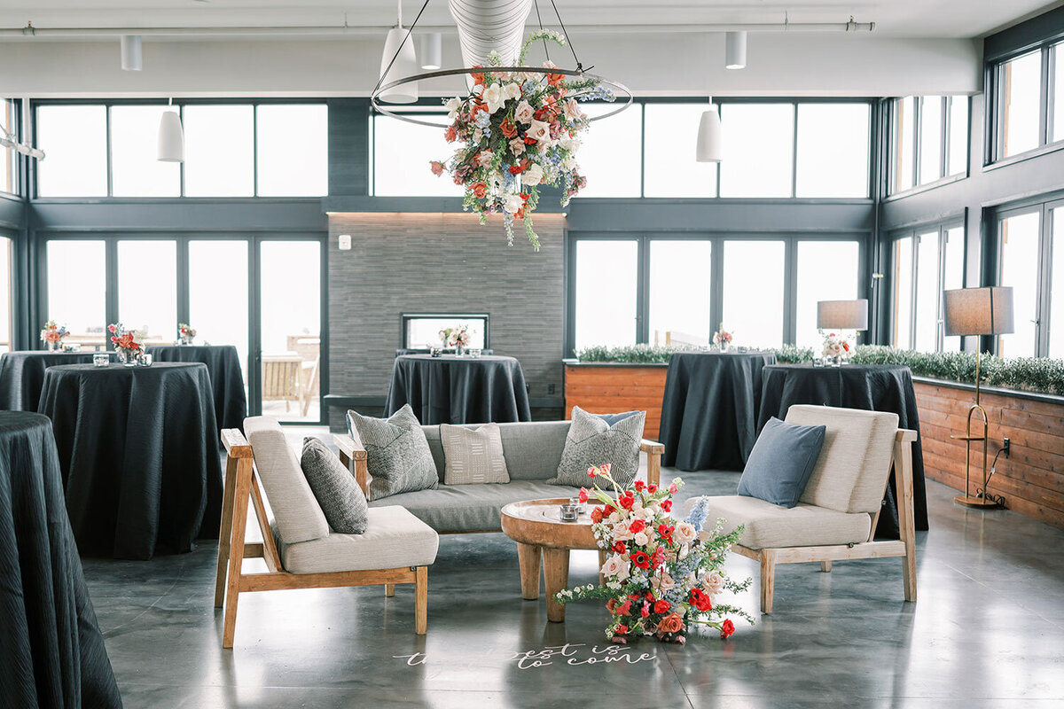Modern lounge setup with neutral seating, bold floral arrangements, and black cocktail tables in a rooftop event space at the Kimpton Armory Hotel in Bozeman, Montana.