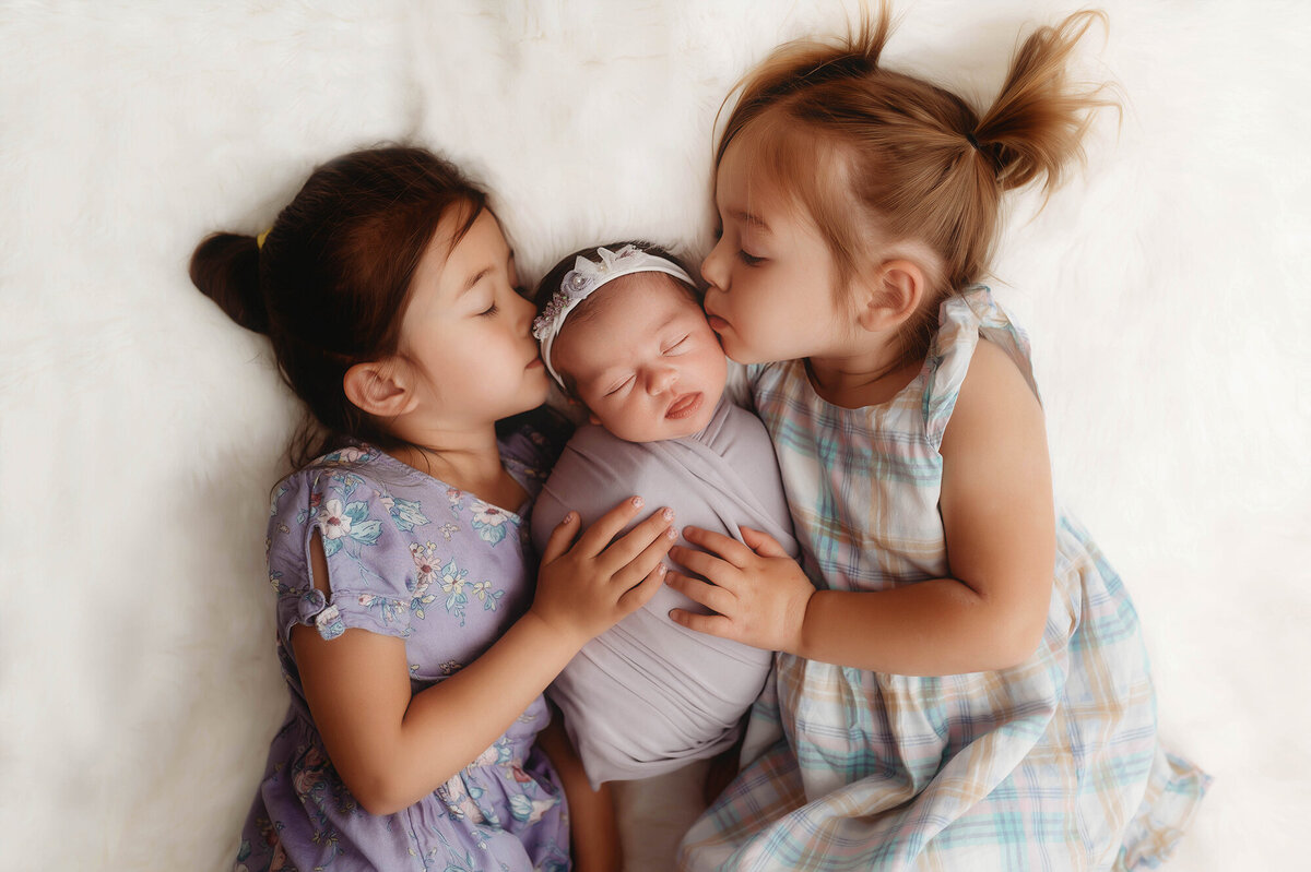 Siblings kiss their baby sister during Newborn Photos in Charleston, SC.