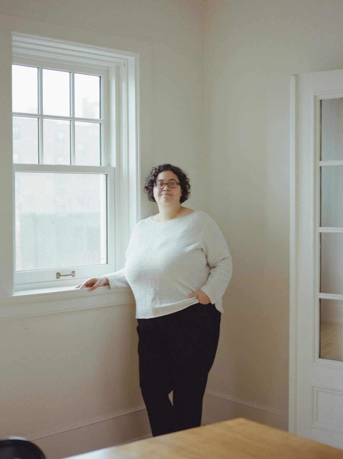 web designer branding photo, woman in white sweater, glasses, curly hair with in white room with character, ALEO Detroit