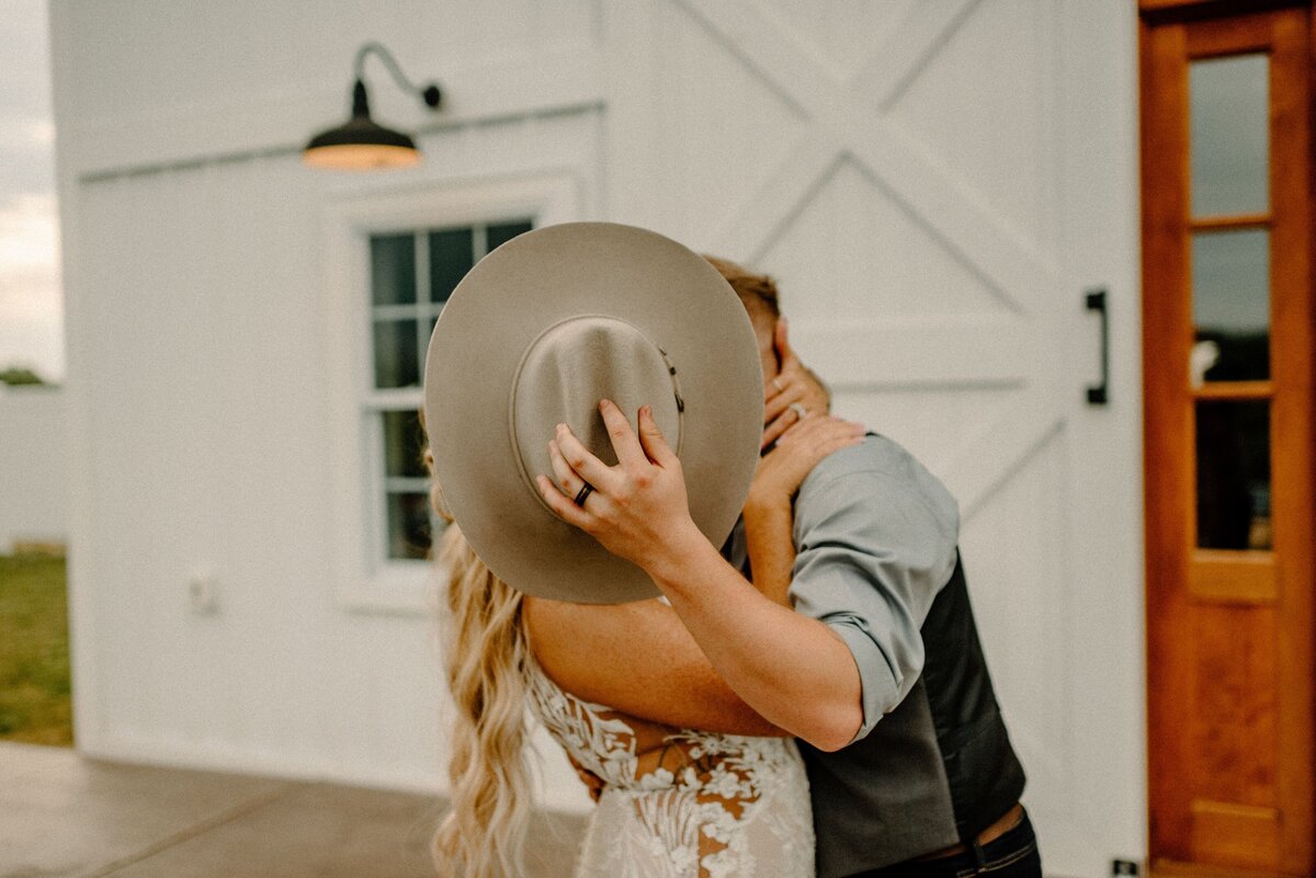 a bride and groom kissing while he holds his cowboy hat up to block the camera