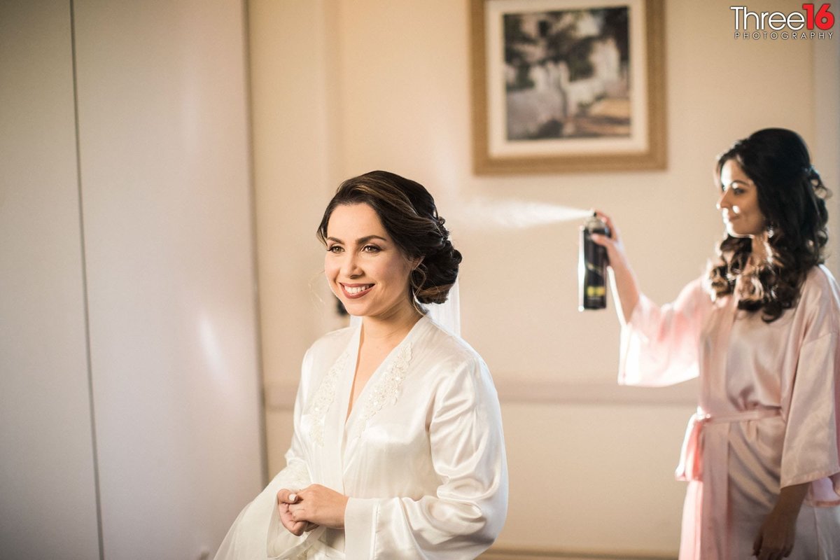 Bride gets a touch of hairspray as she gets dressed for her wedding