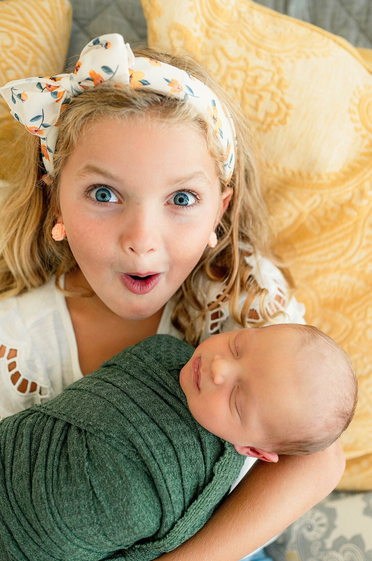 Big sister with surprised face holding baby brother during his Spring Newborn Photography session