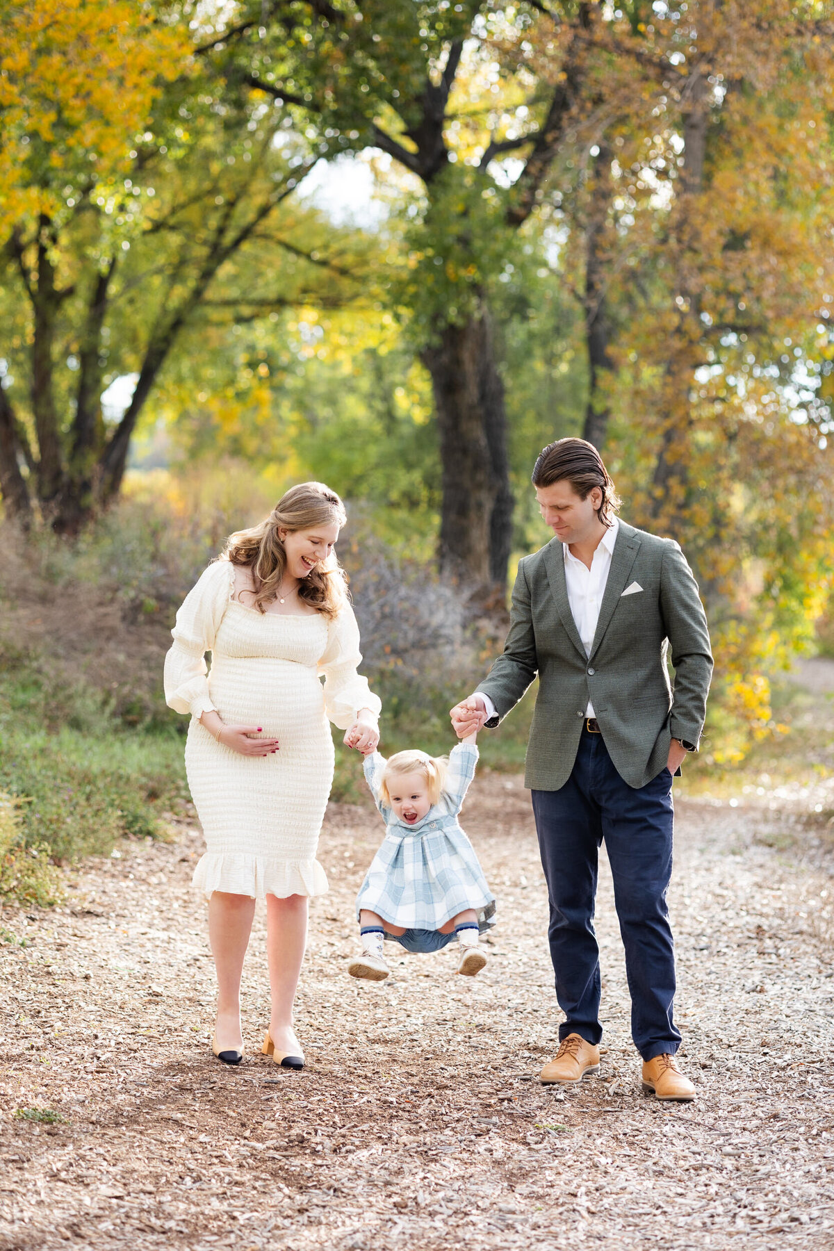 A mom and dad hold their toddler daughter's hands between them as she swings and laughs.