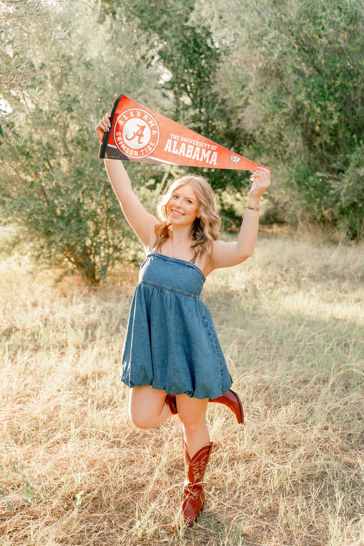 Senior girl holding up alabama penet on grassy field