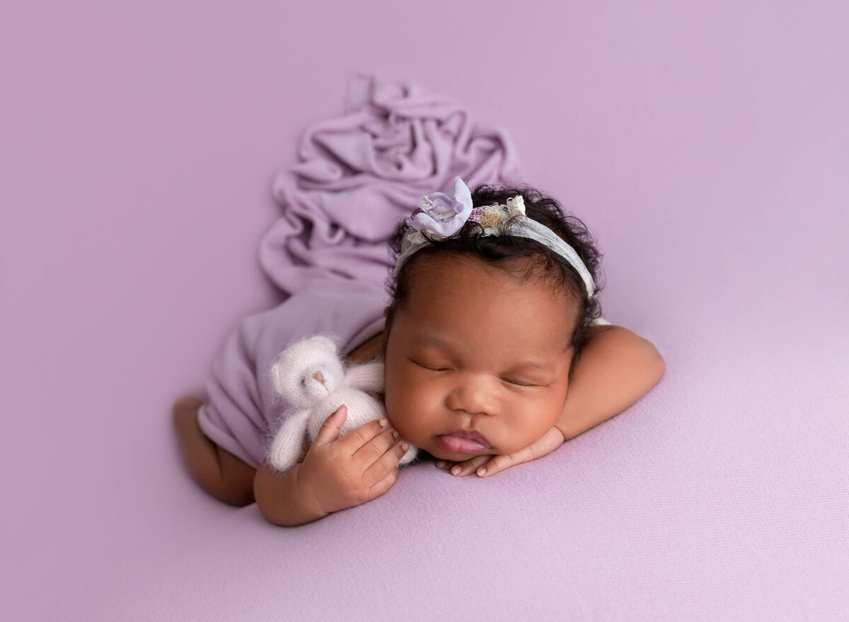 newborn baby girl on lilac blanket holding pink bear toy for newborn photoshoot by NYC newborn photographer 