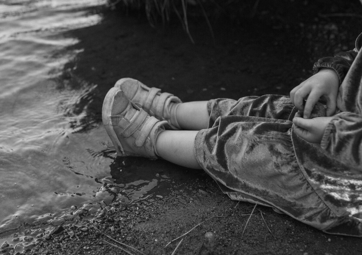 toddler wearing sneakers and velvet dress sitting near the river in Bend, Oregon