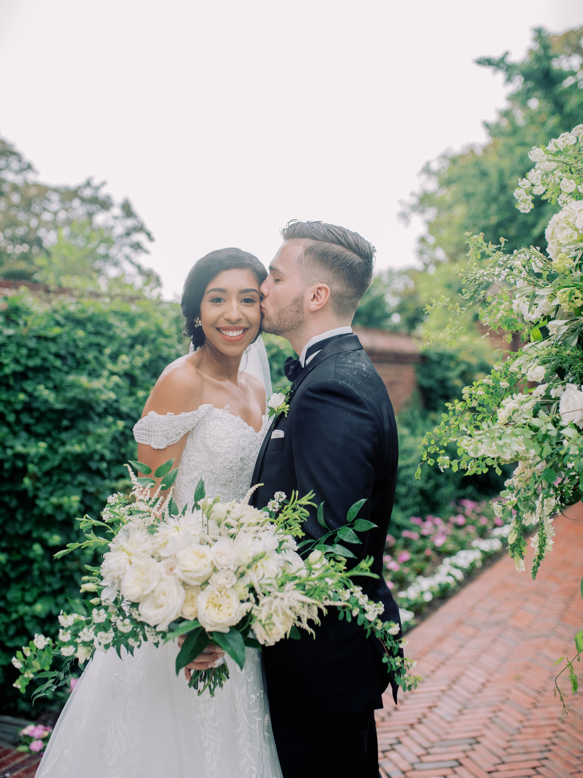 Bride with white bouquet and groom kissing the bride