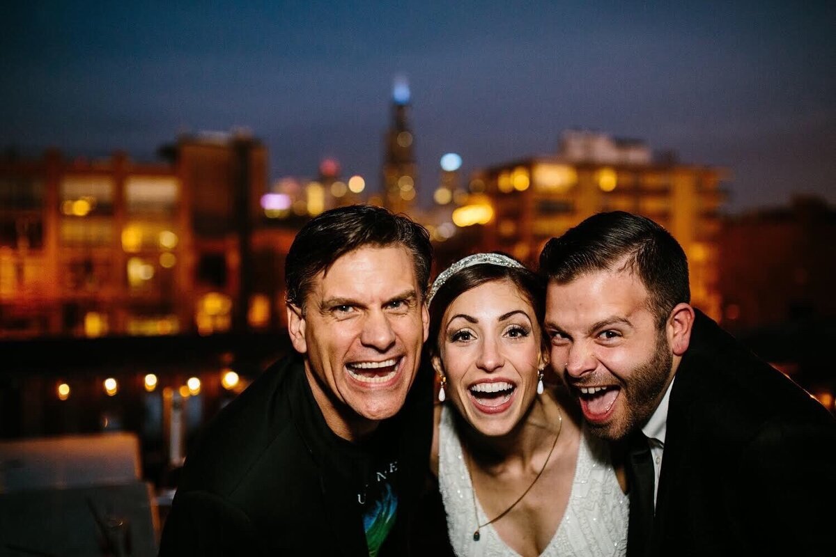 Wedding officiant, Rev Brad Hughes, smiles with excited bride and groom on their wedding day with Chicago skyline in the background