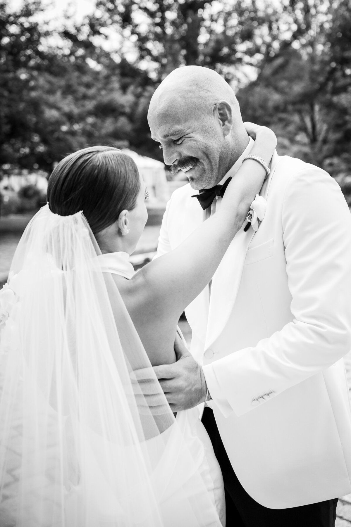 A bride and groom hug and smile at one another during their first look.