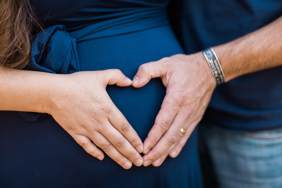 Parents to be place their fingers to each other's forming a heart and places it on her pregnant stomach