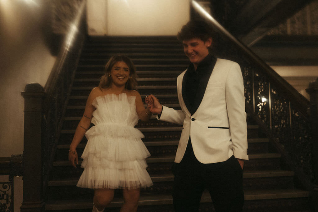 A newlywed couple holding hands and walking down a staircase.