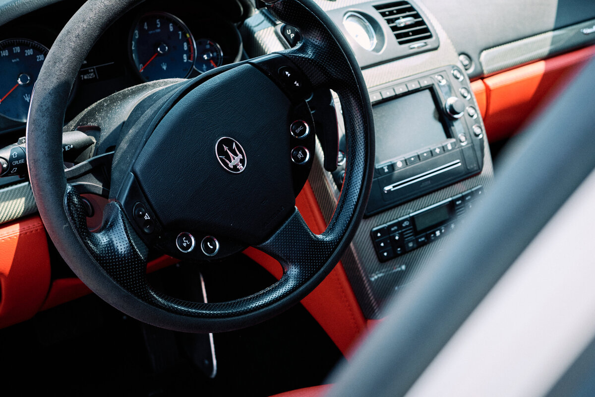 Close-up of a Maserati's luxurious interior showcasing the leather-wrapped steering wheel, carbon fiber accents, and sporty red trim.