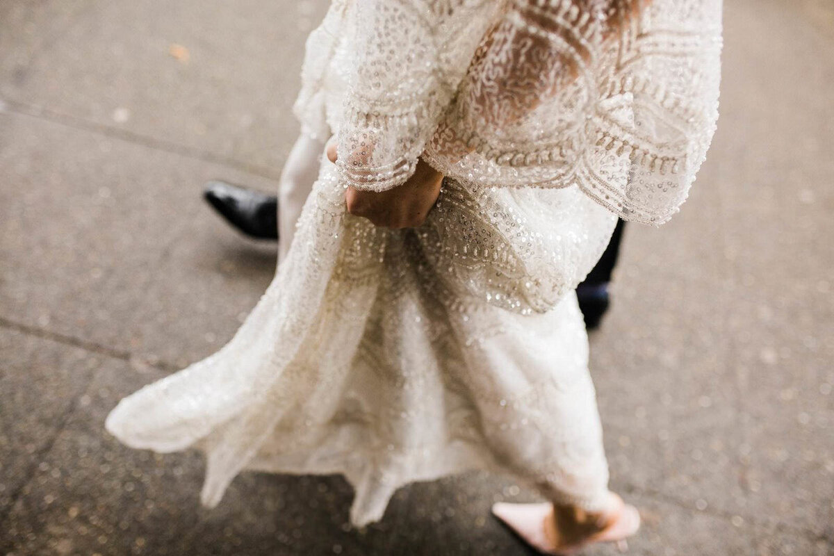 A bride gathers her beaded wedding gown to walk through across a sidewalk in Seattle
