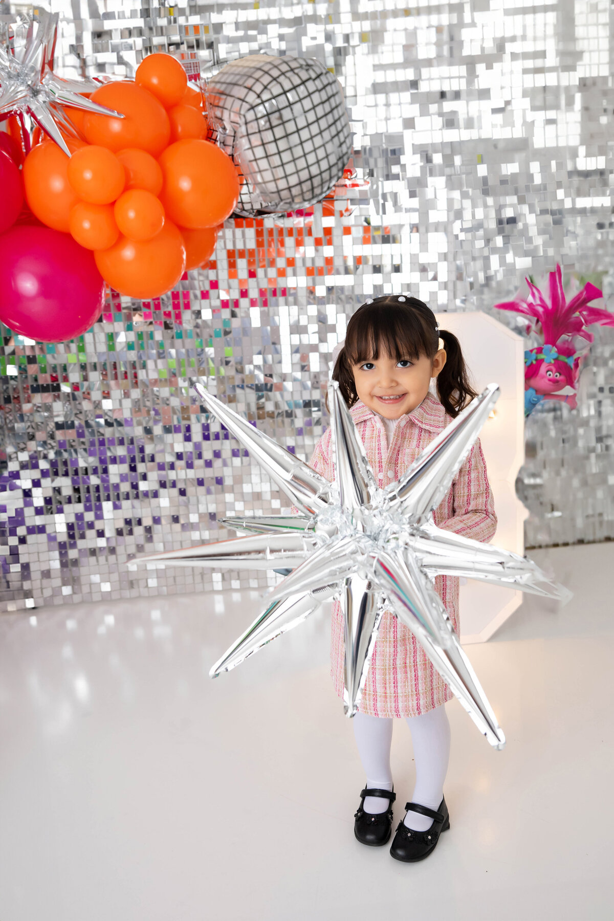 Smiling child holds a metallic star balloon near a shimmering backdrop.