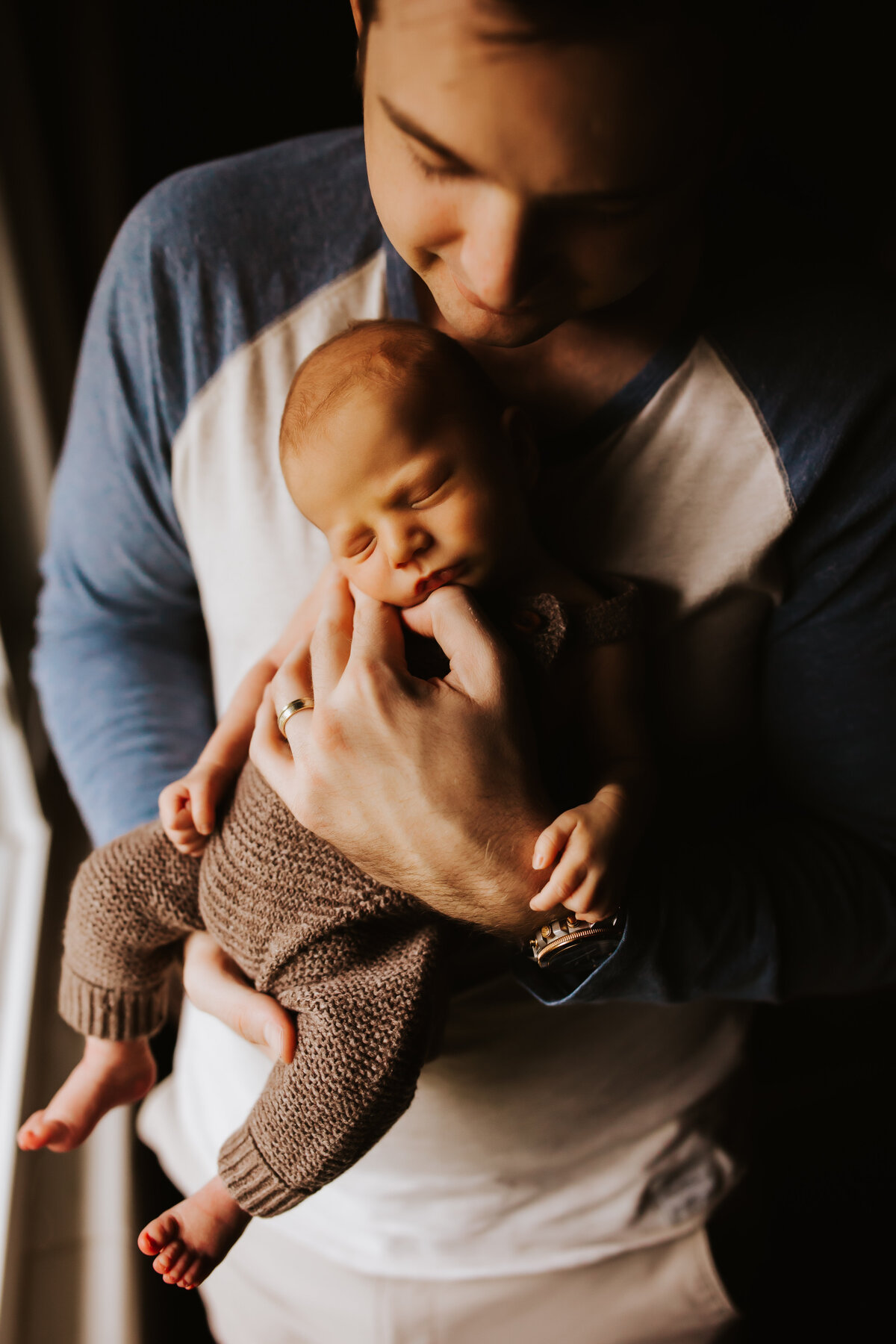 a father cradling his newborn son in front of natural light
