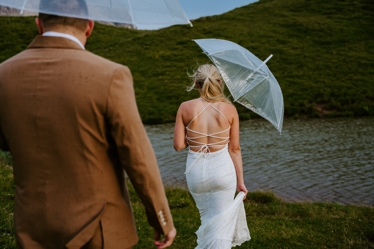 Bride walking with clear umbrella by mountain pond