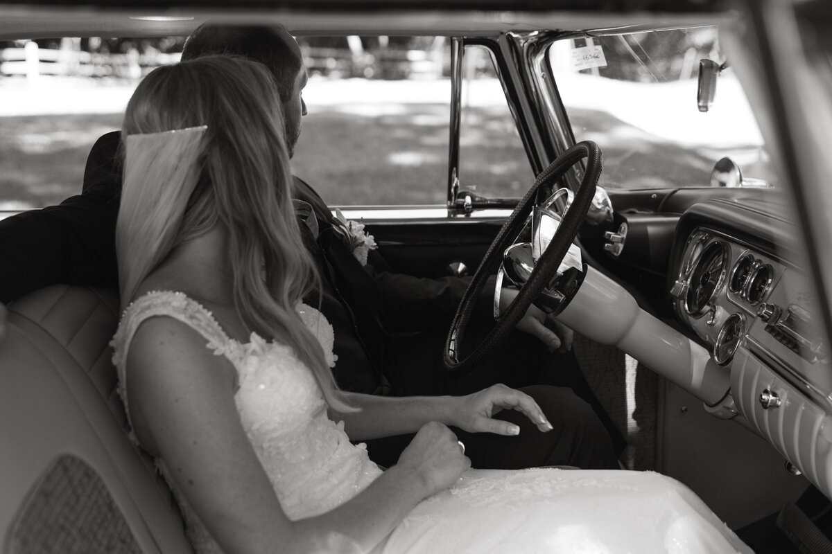 bride and groom driving away in old car