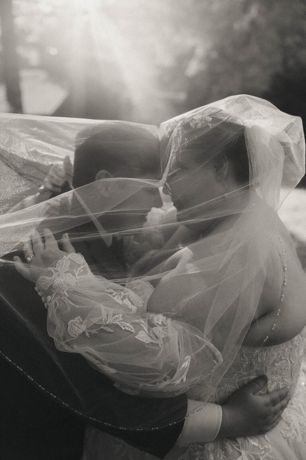 A couple embracing under a wedding veil at their outdoor lake wedding.