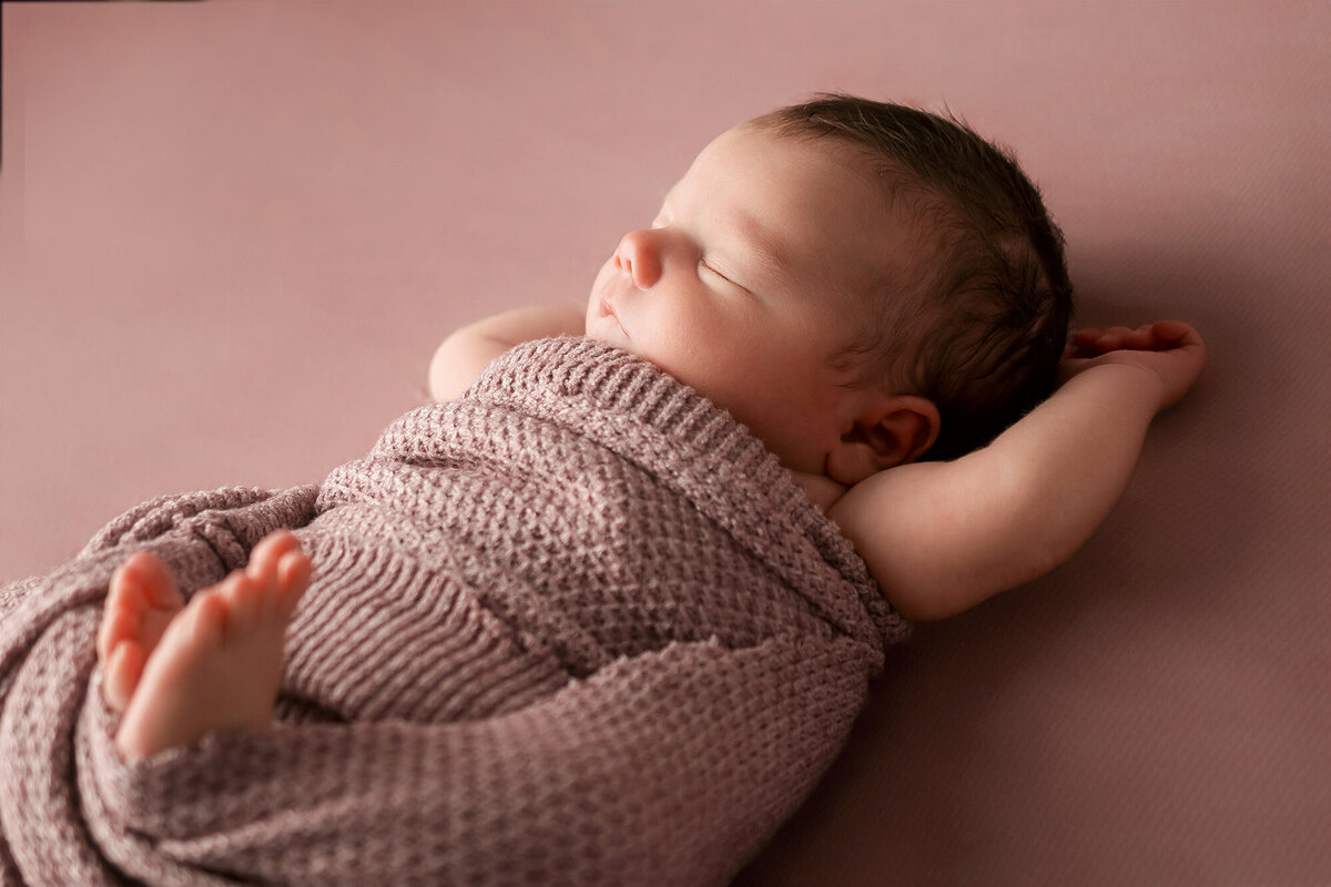 A baby sleeps on back with arms up in knit swaddle