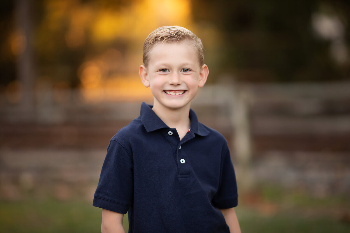 A smiling young boy is captured by a Dallas family photographer during an outdoor family portrait session.