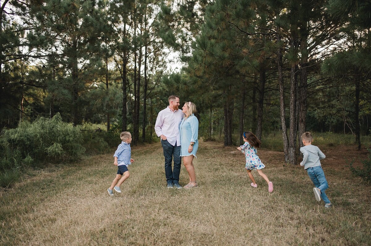 Parents hugging each other while 3 kids run circles around them by Cypress Family Photographer