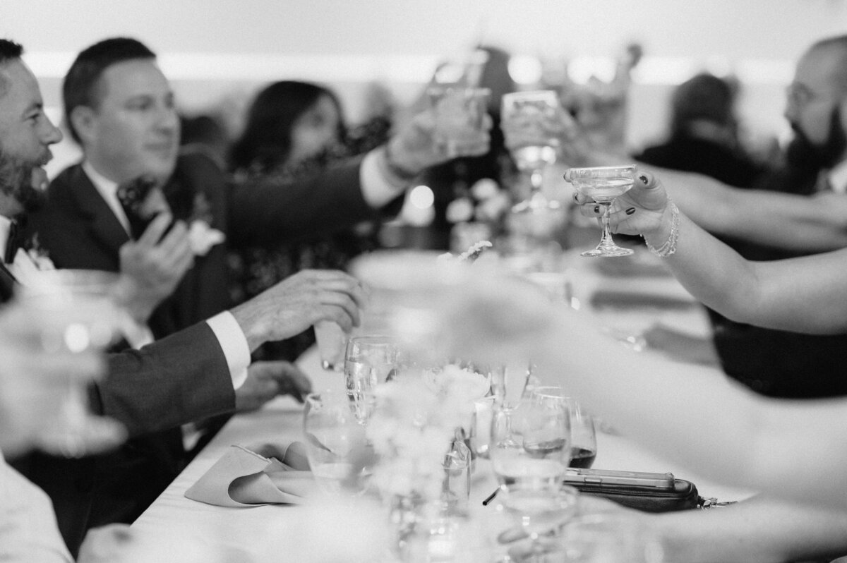 Guests cheers and clink glasses at a wedding. Photo by Anna Brace, a Nebraska Wedding photographer.